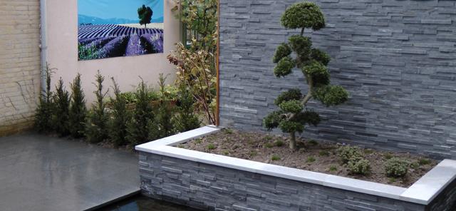 Strakke antraciet plantenbak met bonsai tegen leistenen wand